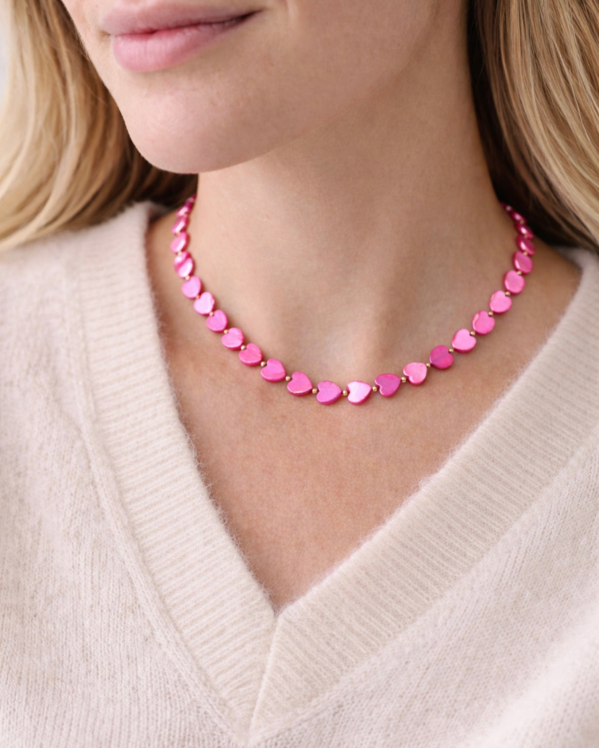 Person wearing a pink heart-shaped beaded necklace against a neutral background