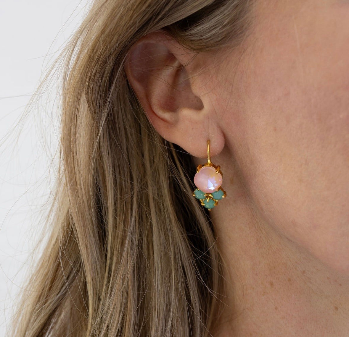 Close-up of an ear wearing a gold earring with a pink gemstone and a smaller cluster of green at the bottom.