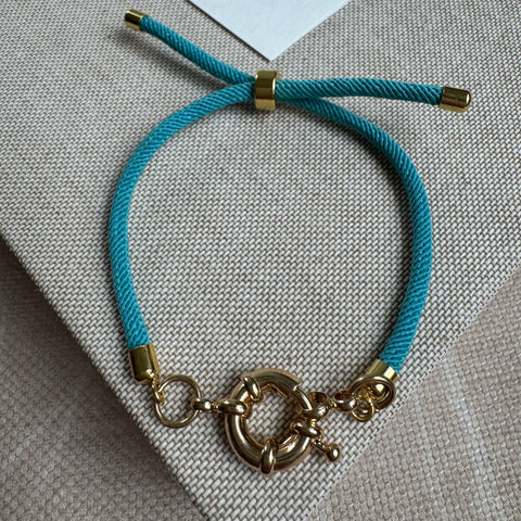 Picture of a teal slider bracelet. Bracelet has gold accent pieces and a gold toggle clasp at it's center.