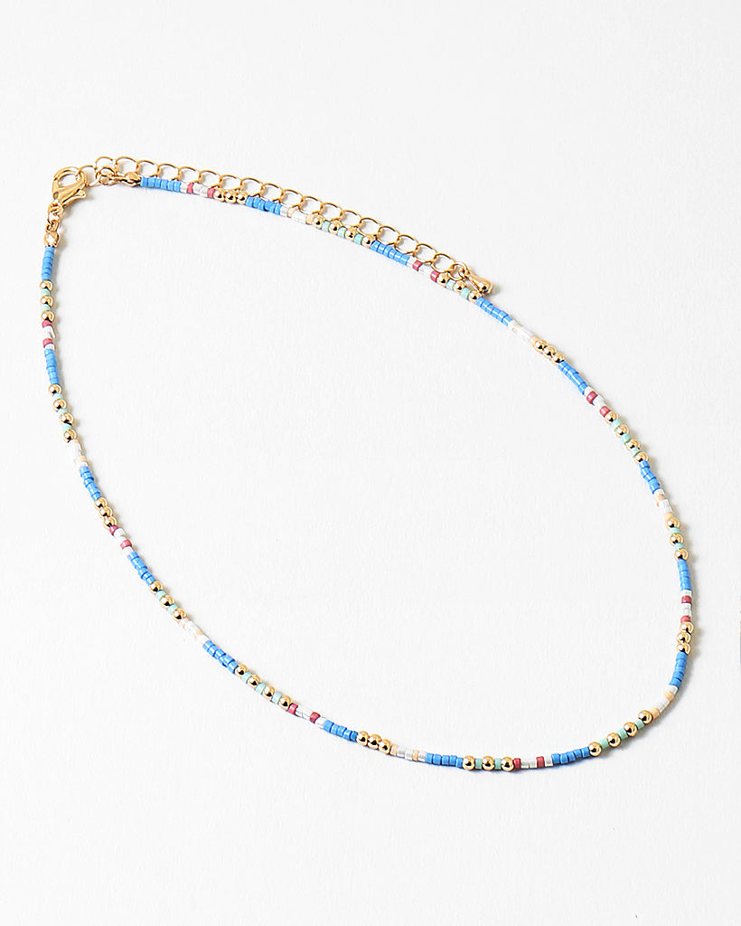 Delicate necklace with blue, white and gold beads and gold chain on a white background
