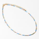 Delicate necklace with blue, white and gold beads and gold chain on a white background