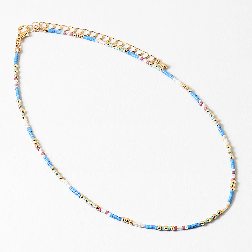 Delicate necklace with blue, white and gold beads and gold chain on a white background