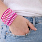 Hand wearing multiple pink beaded bracelets with a white shirt and blue jeans.