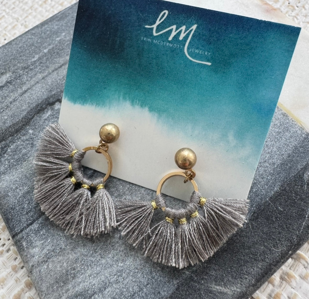 Gray tassel earrings on a card with 'EM' branding