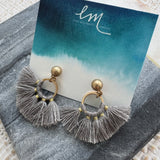 Gray tassel earrings on a card with 'EM' branding