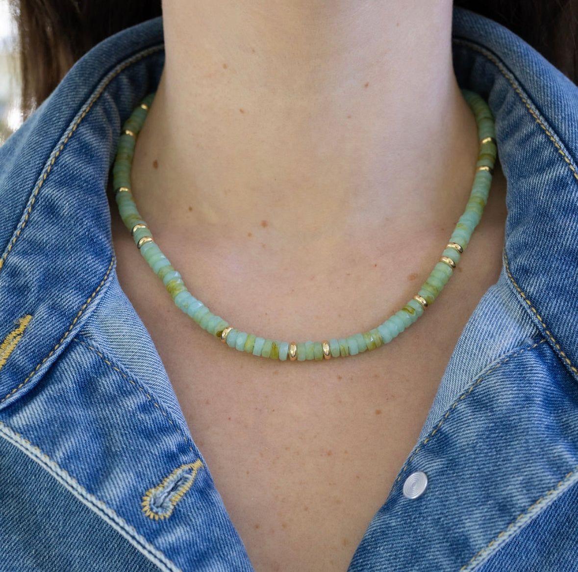 Person wearing a green beaded necklace with gold spacers beads and a denim jacket