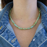 Person wearing a green beaded necklace with gold spacers beads and a denim jacket