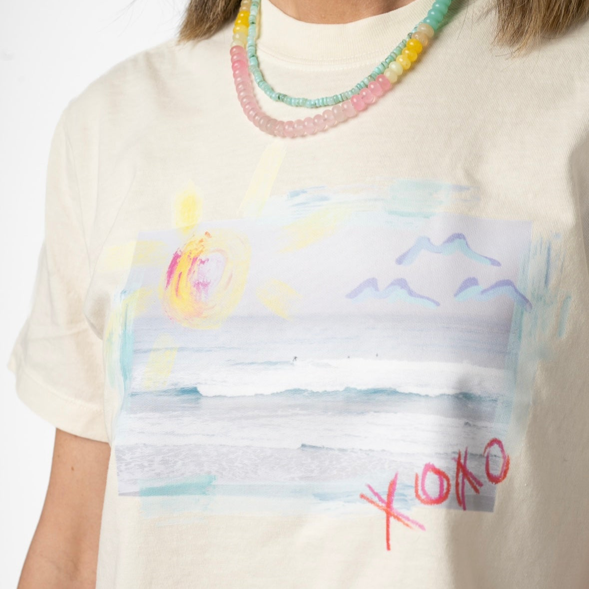 Person wearing a white t-shirt with a colorful abstract Beach design and 'XOXO' text.