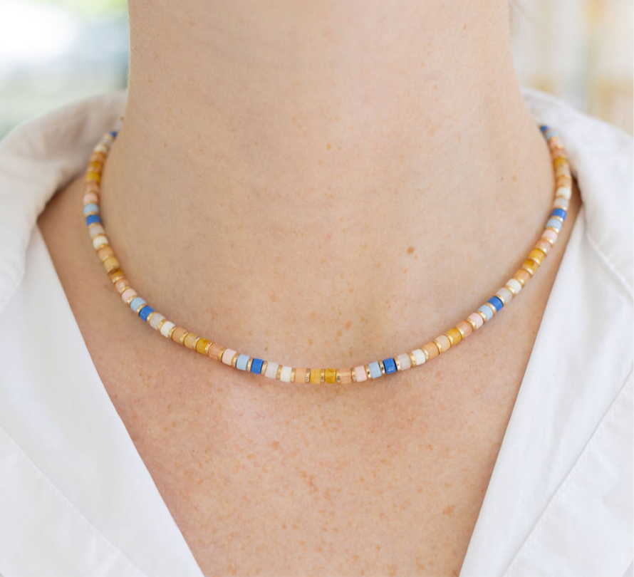 Model wearing a dainty bead necklace in orange, tans, white, teal and blue beads.