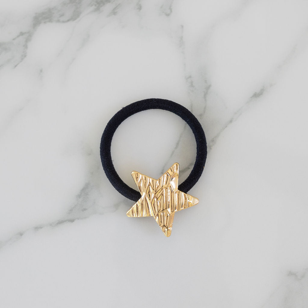 Black hair tie with a gold star-shaped clip on a marble background