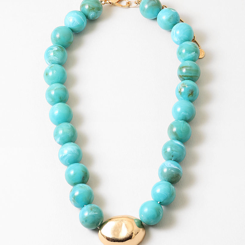 Chunky turquoise beaded necklace with a large oval gold bead and gold clasp on a white background