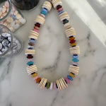 Necklace with thin wooden disc beads and multicolored beads on a marble surface