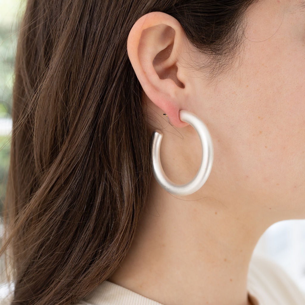 Picture of model wearing a large white silver matte hoop earrings.