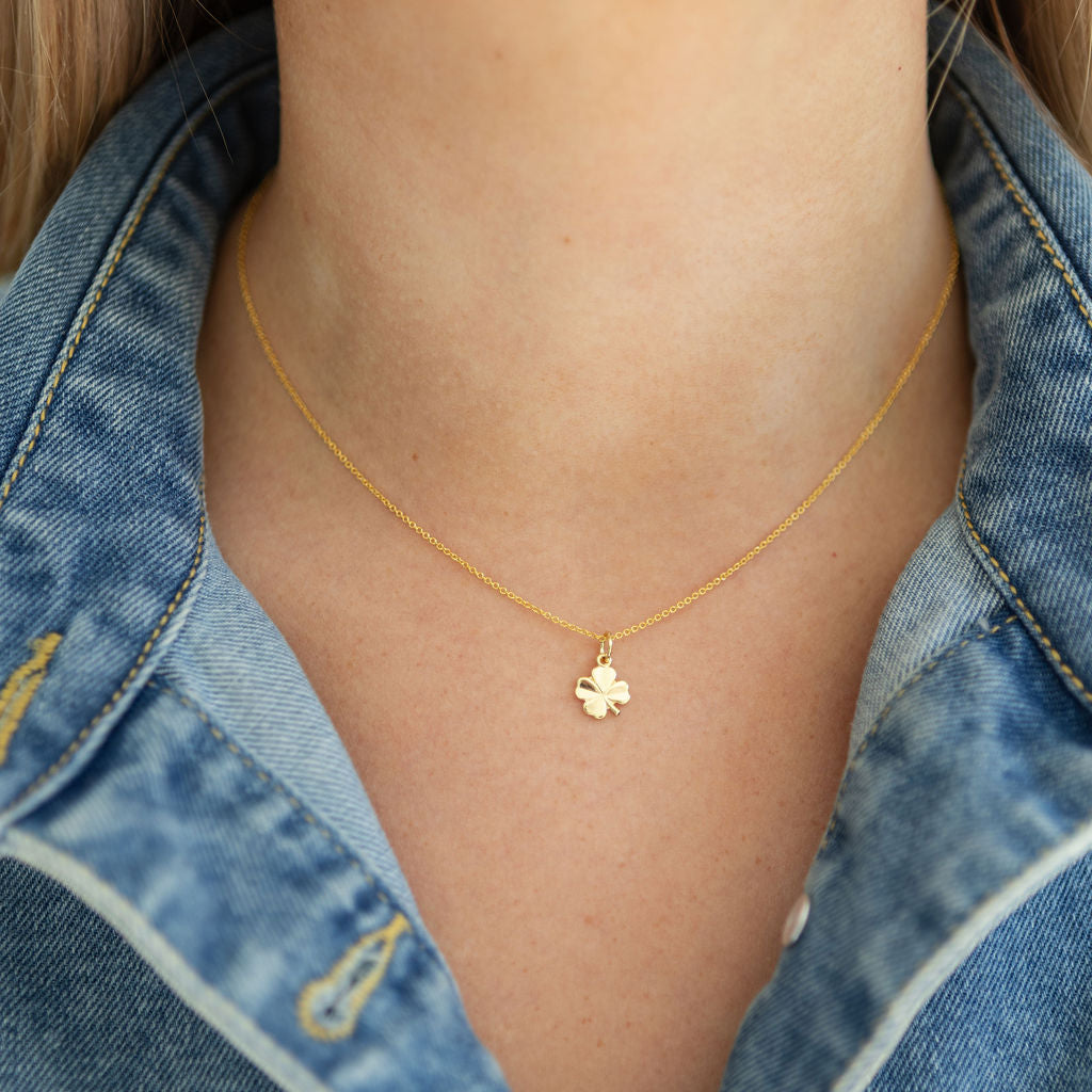 Gold necklace with a clover pendant worn by a person in a denim jacket.