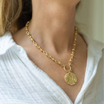 Woman wearing a gold chunky chained necklace with a large gold medallion attached to it