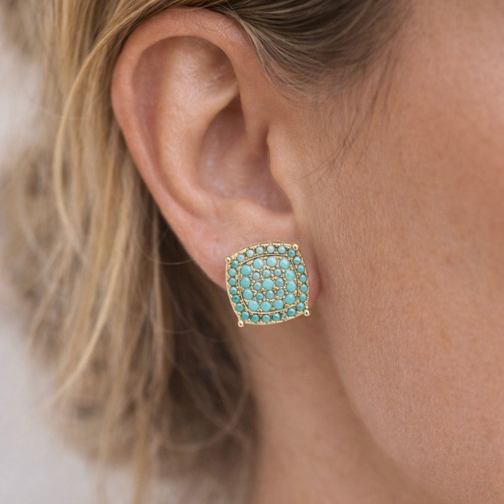 Close-up of an ear wearing a turquoise square earring with gold accents.