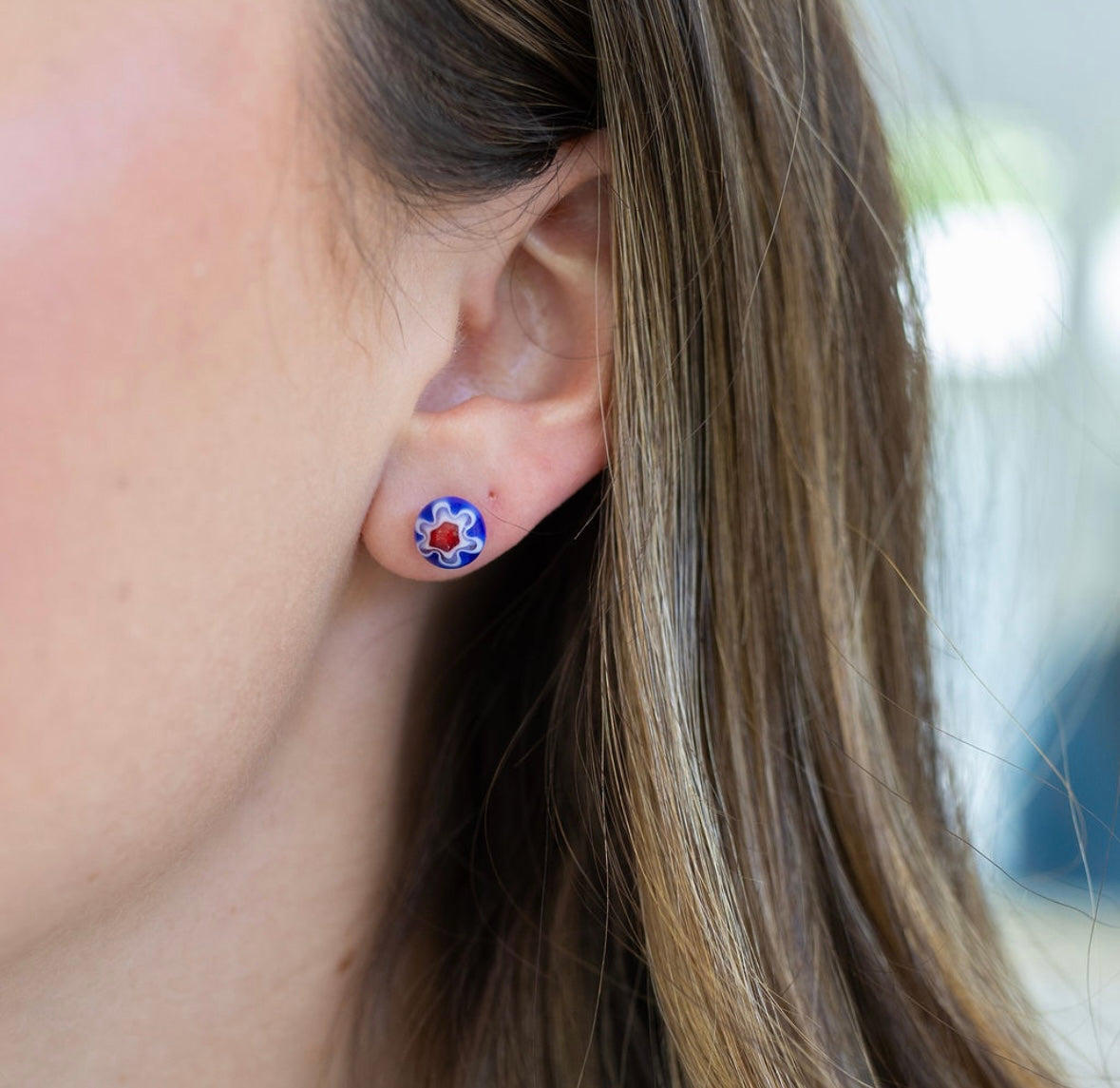 Close-up of an ear wearing a floral blue and red stud earring with a blurred background