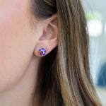 Close-up of an ear wearing a floral blue and red stud earring with a blurred background