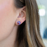 Close-up of an ear wearing a floral blue and red stud earring with a blurred background