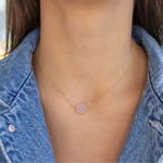 Gold necklace with a pink pendant worn by a person in a denim jacket.