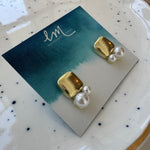 Picture of a pair of gold square studs with two pearls of varying sizes attached to the base of them.