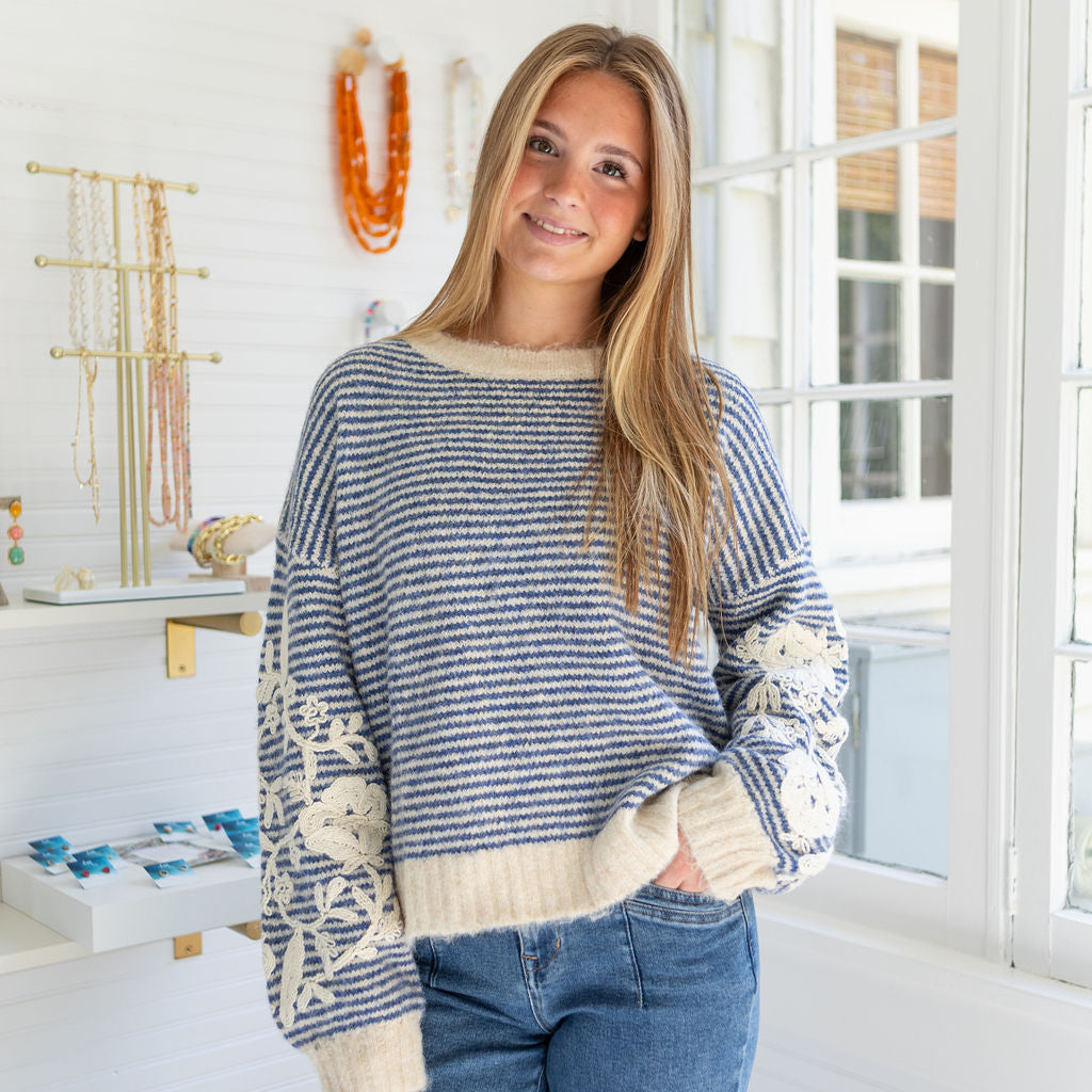 Woman wearing a blue and white patterned sweater in a bright room with jewelry in the background