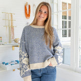 Woman wearing a blue and white patterned sweater in a bright room with jewelry in the background