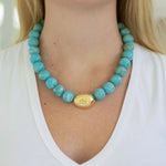 Chunky turquoise beaded necklace with a gold accent bead worn by a person in a white shirt.