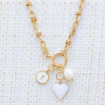 Picture of gold toggle chain with a white heart charm, white disc charm with a cross at the center and a fresh water pearl charm.