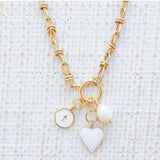 Picture of gold toggle chain with a white heart charm, white disc charm with a cross at the center and a fresh water pearl charm.