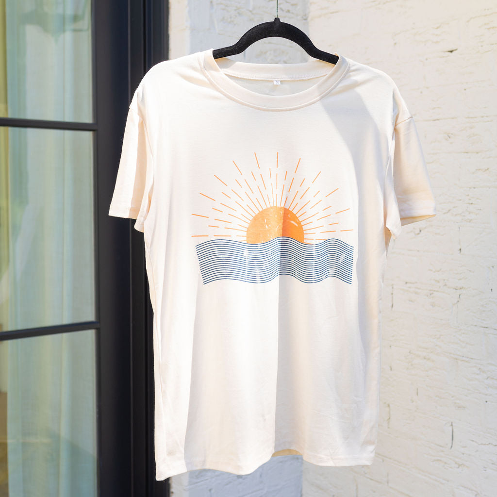 A plain white shirt with an image of an orange sun rising over an ocean 