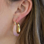 Close-up of an ear wearing gold hoop earrings with pink resin coating against a blurred background