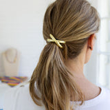 Person with a ponytail held by a gold hair band against a neutral background