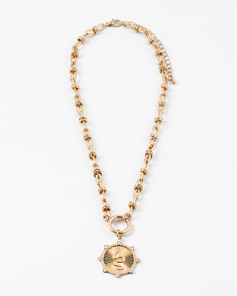 Gold necklace with a large gold clasp and a circular textured pendant on a white background