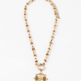 Gold necklace with a large gold clasp and a circular textured pendant on a white background