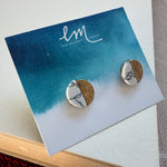 Picture of a pair of studs in a blue and white earring holder. Earrings are half white and black marble and half textured gold.