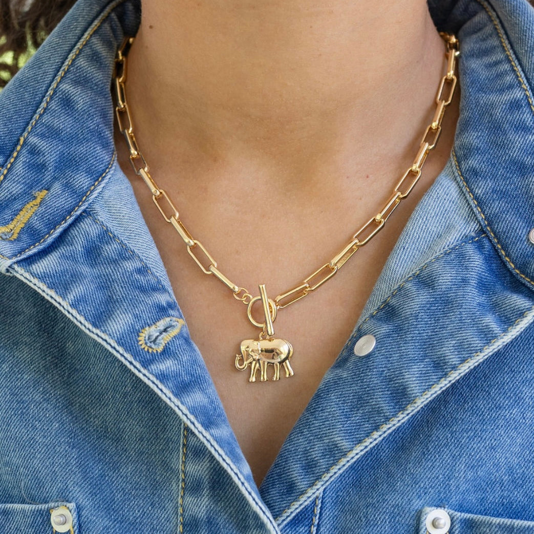 Gold rectangle chain necklace with a toggle clasp and an elephant pendant worn by a person in a denim jacket.