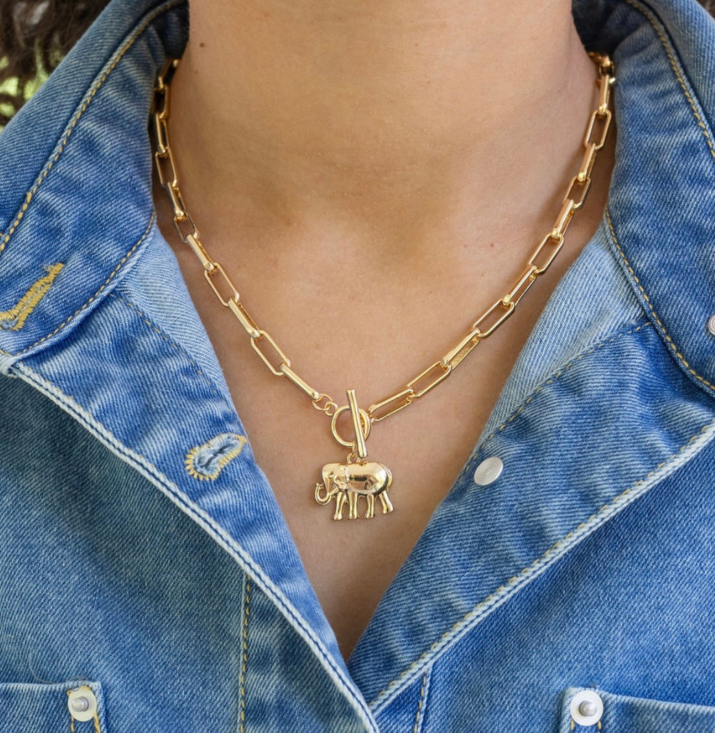 Gold rectangle chain necklace with a toggle clasp and an elephant pendant worn by a person in a denim jacket.