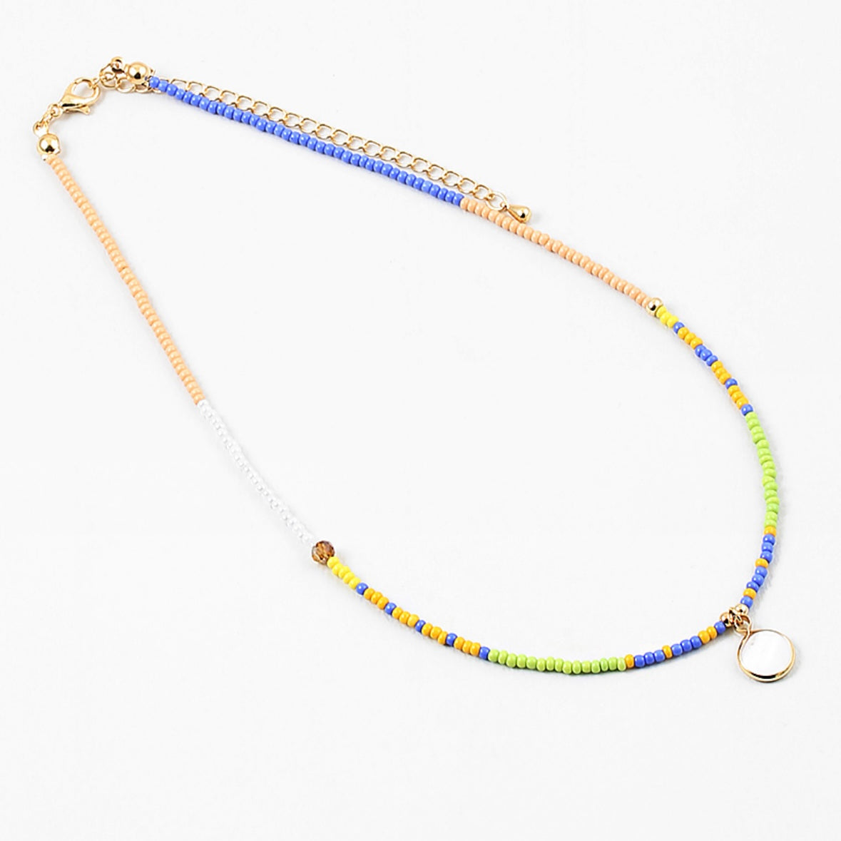 Dainty bead necklace in colors of blue, yellow, tan, green and white. Necklace has a small white disc pendant.