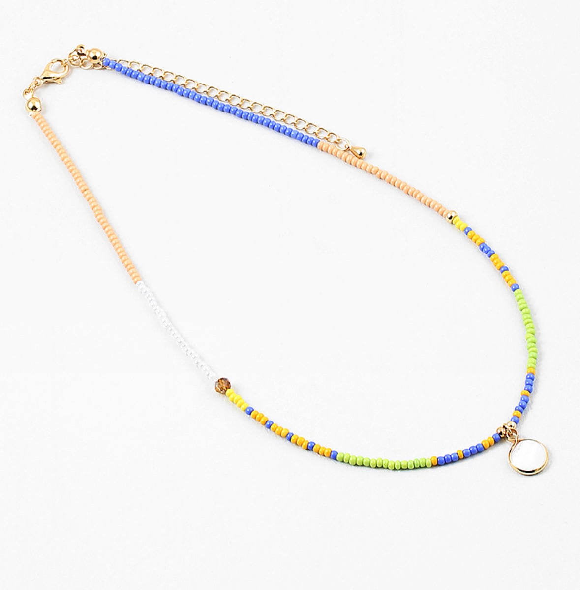 Dainty bead necklace in colors of blue, yellow, tan, green and white. Necklace has a small white disc pendant.