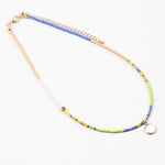 Dainty bead necklace in colors of blue, yellow, tan, green and white. Necklace has a small white disc pendant.