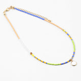 Dainty bead necklace in colors of blue, yellow, tan, green and white. Necklace has a small white disc pendant.