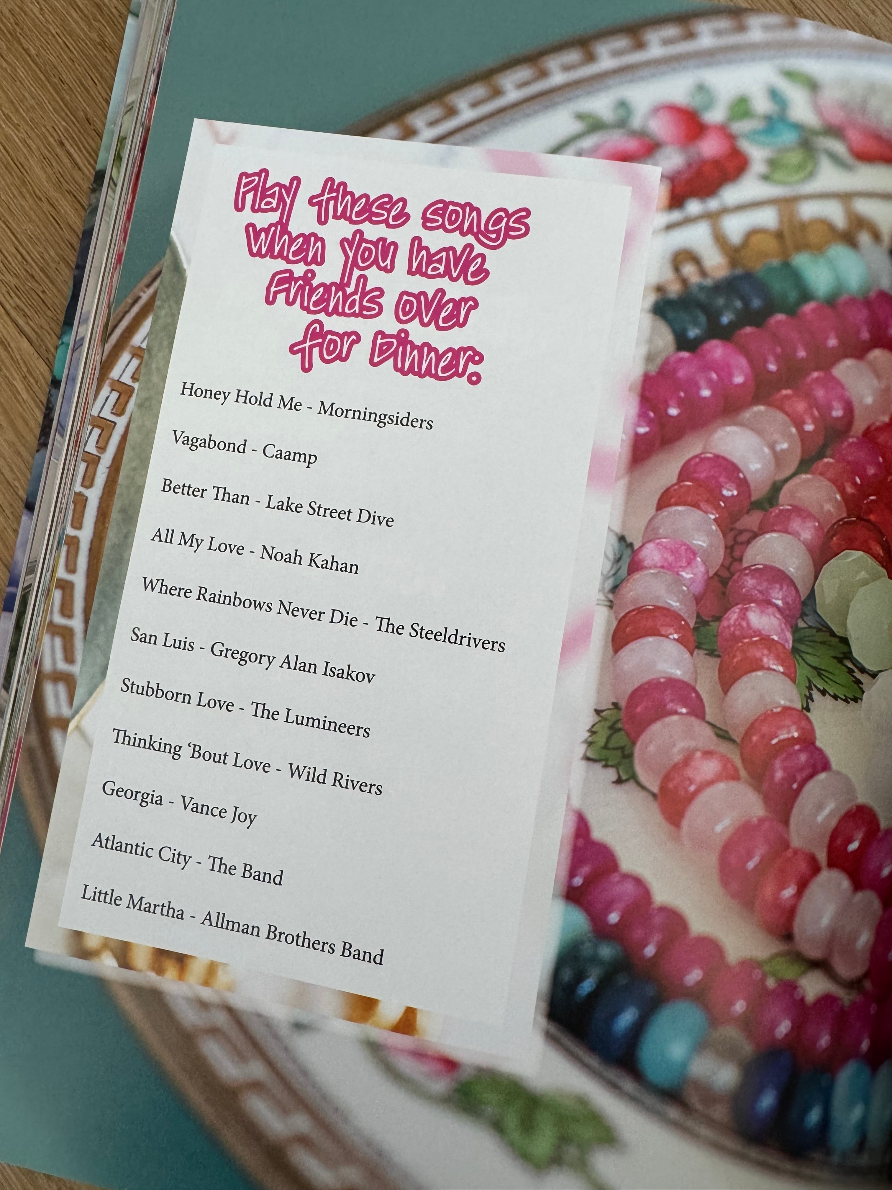Magazine page of colorful beads on a decorative plate with a paper card featuring playlist text.