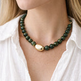 Green beaded necklace with a large central gold bead and gold clasp worn by a person in a white shirt.
