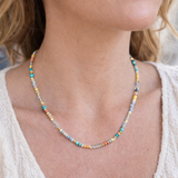 Multicolored beaded necklace in blues, yellows, clears and corals on a person wearing a white top.