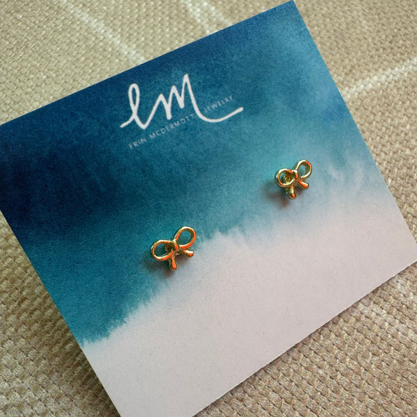 Picture of a blue and white earring holder displaying tiny delicate gold bow earrings.