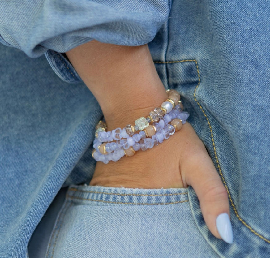Person wearing multiple blue beaded bracelets on a denim background