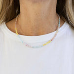 Close-up of a person wearing a delicate light colored beaded necklace on a plain background