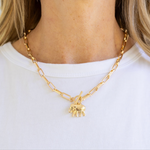 Woman wearing a large gold rectangle chain necklace with a toggle clasp and a gold elephant pendant.
