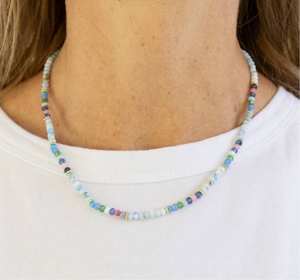 Multicolored bead necklace in blues, greys and whites on a woman with a white Tshirt.